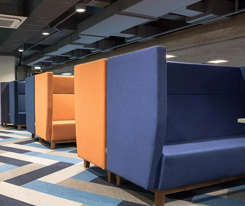 Tall booths made up of blue and orange chairs on patterned carpet